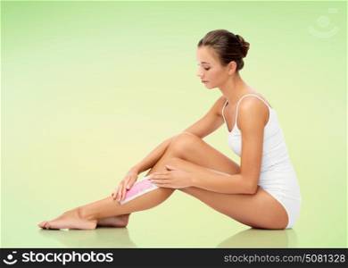 beauty, hair removal and people concept - beautiful woman applying depilatory wax strip to her leg skin over green background. woman removing leg hair with depilatory wax strip