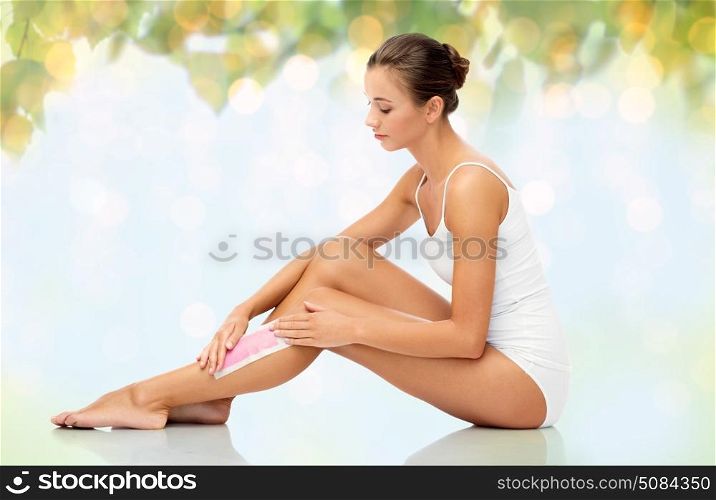 beauty, hair removal and people concept - beautiful woman applying depilatory wax strip to her leg skin over natural green background and lights. woman removing leg hair with depilatory wax strip. woman removing leg hair with depilatory wax strip