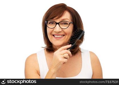 beauty, haircare and old people concept - portrait of smiling senior woman in glasses brushing hair by hairbrush over white background. portrait of senior woman in glasses brushing hair