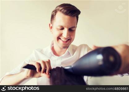 beauty, hairstyle and people concept - happy stylist with fan and brush making blow-dry to client at hair salon