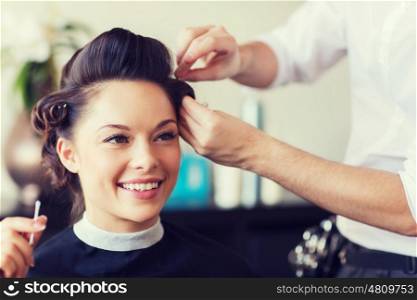 beauty, hairstyle and people concept - happy young woman with hairdresser making hairdo at salon