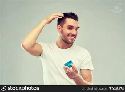 beauty, hairstyle, haircare and people concept - happy young man styling his hair with wax or gel over gray background. happy young man styling his hair with wax or gel