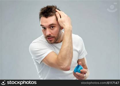 beauty, hairstyle, haircare and people concept - happy young man styling his hair with wax or gel over gray background