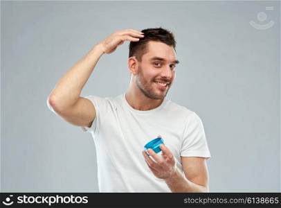 beauty, hairstyle, haircare and people concept - happy young man styling his hair with wax or gel over gray background