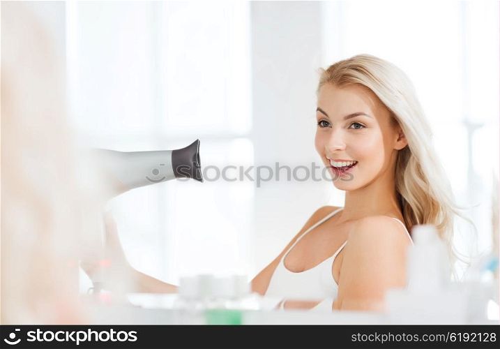 beauty, hairstyle, morning and people concept - smiling young woman with fan blow drying her hair looking to mirror at home bathroom