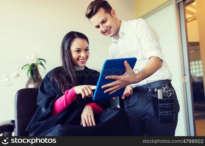 beauty, hairstyle, technology and people concept - happy young woman and stylist with tablet pc computer at salon