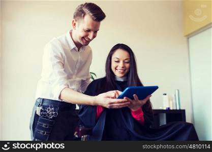 beauty, hairstyle, technology and people concept - happy young woman and stylist with tablet pc computer at salon