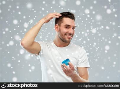 beauty, hairstyle, winter, christmas and people concept - happy young man styling his hair with wax or gel over snow on gray background