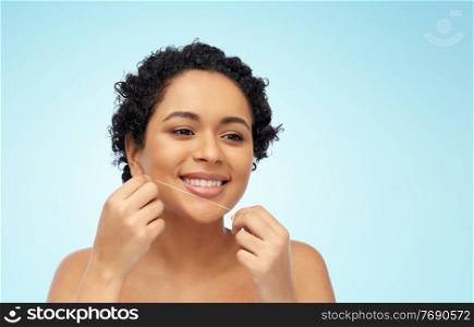 beauty, health and people concept - close up of of happy smiling young african american woman cleaning teeth with dental floss over blue background. african woman cleaning teeth with dental floss
