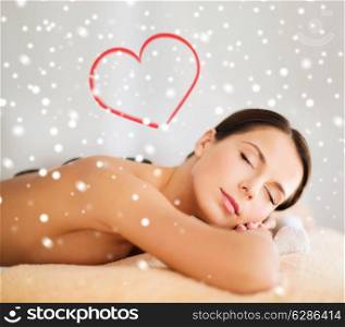 beauty, health, holidays, people and spa concept - beautiful woman in spa salon getting hot stones massage over snowflakes with red heart shape background