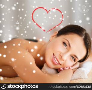 beauty, health, holidays, people and spa concept - beautiful woman in spa salon getting hot stones massage over snowflakes with red heart shape background