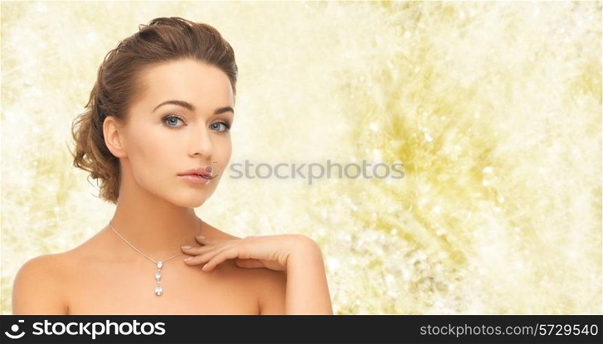 beauty, holidays, people and jewelry concept - woman wearing shiny diamond pendant over yellow lights background
