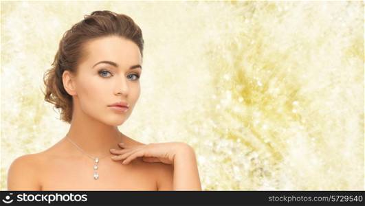 beauty, holidays, people and jewelry concept - woman wearing shiny diamond pendant over yellow lights background
