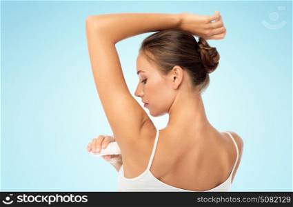 beauty, hygiene and people concept - beautiful young woman applying antiperspirant or stick deodorant over blue background. woman with antiperspirant deodorant over white