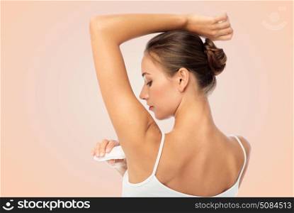beauty, hygiene and people concept - beautiful young woman applying antiperspirant or stick deodorant over beige background. woman with antiperspirant deodorant over white. woman with antiperspirant deodorant over white