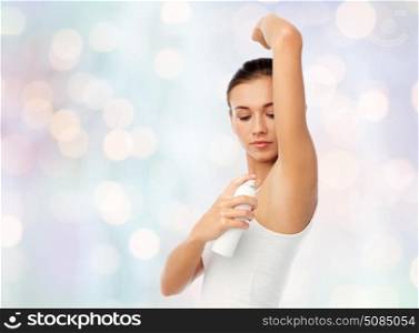 beauty, hygiene and people concept - beautiful young woman applying antiperspirant or spray deodorant over blue lights background. woman with antiperspirant deodorant over white. woman with antiperspirant deodorant over white
