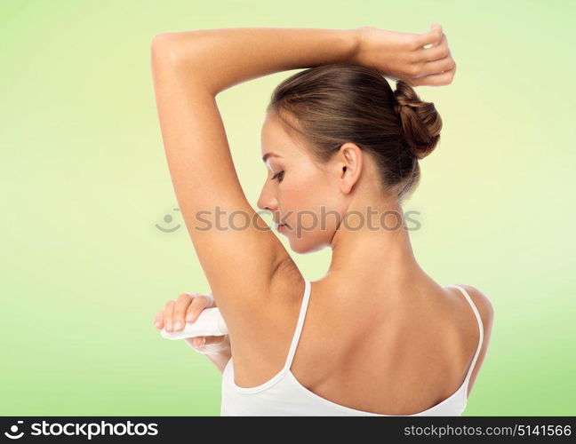 beauty, hygiene and people concept - beautiful young woman applying antiperspirant or stick deodorant over green natural background. woman with antiperspirant deodorant over white