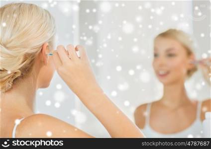 beauty, hygiene and people concept - close up of smiling young woman cleaning ear with cotton swab and looking to mirror at home bathroom over snow