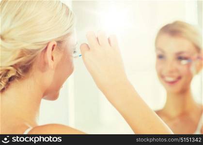 beauty, hygiene and people concept - close up of smiling young woman fixing makeup with cotton swab and looking to mirror at home bathroom. woman fixing makeup with cotton swab at bathroom