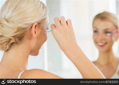 beauty, hygiene and people concept - close up of smiling young woman fixing makeup with cotton swab and looking to mirror at home bathroom