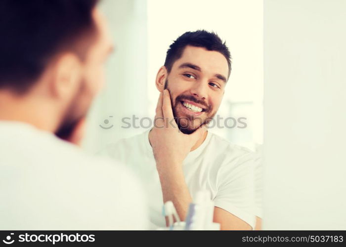 beauty, hygiene and people concept - smiling young man looking to mirror at home bathroom. happy young man looking to mirror at home bathroom