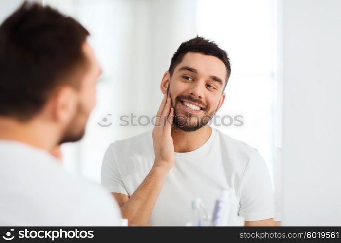 beauty, hygiene and people concept - smiling young man looking to mirror at home bathroom