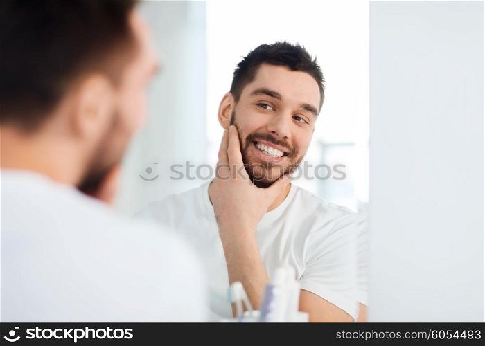 beauty, hygiene and people concept - smiling young man looking to mirror at home bathroom