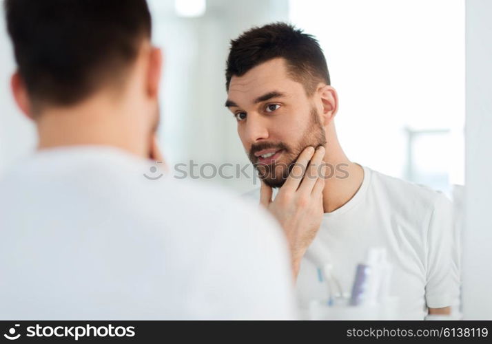 beauty, hygiene and people concept - smiling young man looking to mirror at home bathroom