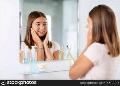 beauty, hygiene and people concept - teenage girl looking in mirror at bathroom. teenage girl looking in mirror at bathroom