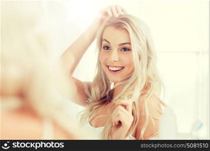 beauty, hygiene, hairstyle, morning and people concept - smiling young woman looking to mirror at home bathroom. happy young woman looking to mirror at bathroom