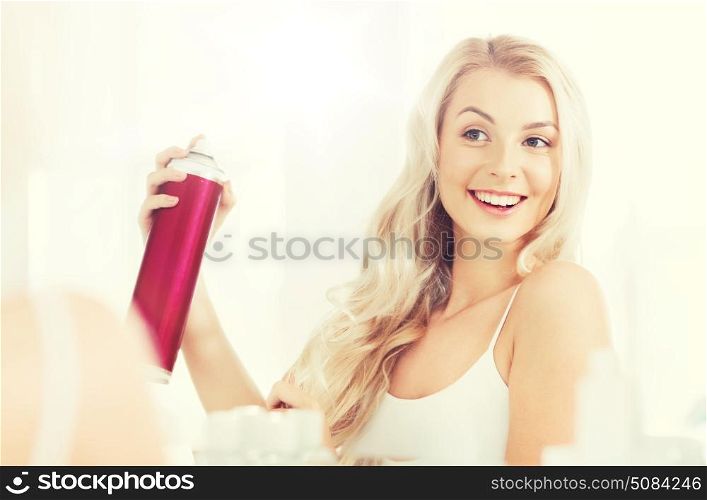 beauty, hygiene, hairstyle, morning and people concept - smiling young woman with hairspray styling her hair and looking to mirror at home bathroom. woman with hairspray styling her hair at bathroom. woman with hairspray styling her hair at bathroom