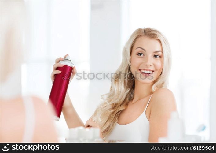 beauty, hygiene, hairstyle, morning and people concept - smiling young woman with hairspray styling her hair and looking to mirror at home bathroom