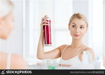 beauty, hygiene, hairstyle, morning and people concept - young woman with hairspray styling her hair and looking to mirror at home bathroom