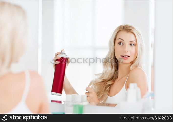 beauty, hygiene, hairstyle, morning and people concept - young woman with hairspray styling her hair and looking to mirror at home bathroom