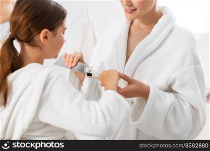 beauty, hygiene, morning and people concept - close up of happy smiling mother and daughter applying toothpaste to toothbrush at bathroom. mother and daughter with toothpaste and toothbrush