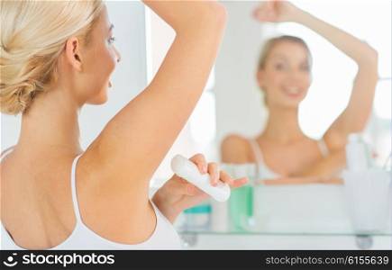 beauty, hygiene, morning and people concept - close up of smiling young woman applying antiperspirant or stick deodorant and looking to mirror at home bathroom