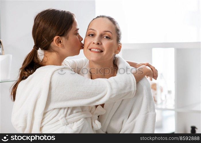 beauty, hygiene, morning and people concept - happy daughter kissing and hugging her smiling mother in bathroom. daughter kissing her smiling mother in bathroom
