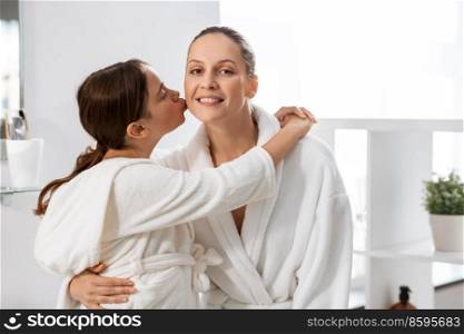 beauty, hygiene, morning and people concept - happy daughter kissing and hugging her smiling mother in bathroom. daughter kissing her smiling mother in bathroom