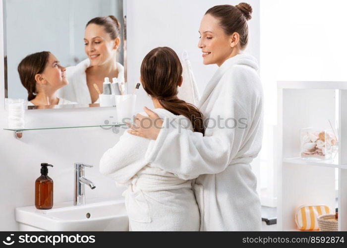 beauty, hygiene, morning and people concept - happy smiling mother and daughter in front of mirror at bathroom. mother and daughter in front of mirror at bathroom