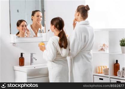 beauty, hygiene, morning and people concept - happy smiling mother and daughter with moisturizer looking to mirror in bathroom. mother and daughter with moisturizer in bathroom