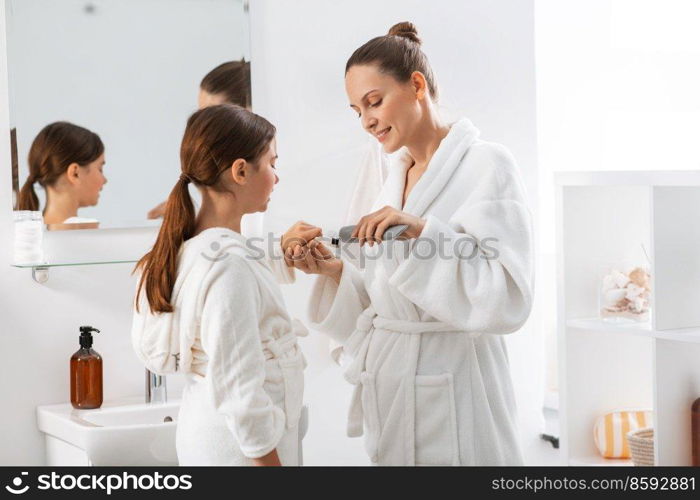 beauty, hygiene, morning and people concept - happy smiling mother and daughter applying toothpaste to toothbrush at bathroom. mother and daughter with toothpaste and toothbrush