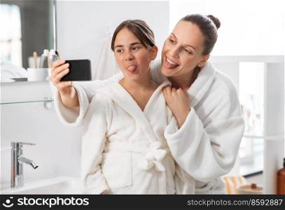 beauty, hygiene, morning and people concept - happy smiling mother and daughter taking selfie with smartphone at bathroom. mother and daughter taking selfie with smartphone