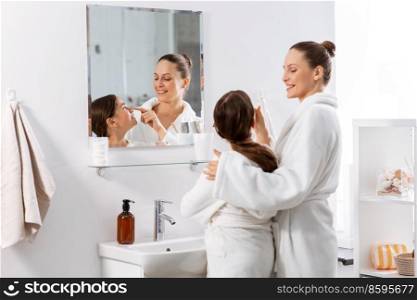 beauty, hygiene, morning and people concept - happy smiling mother and daughter in front of mirror at bathroom. mother and daughter in front of mirror at bathroom