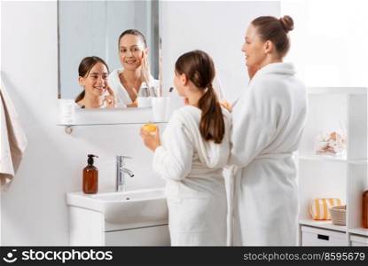 beauty, hygiene, morning and people concept - happy smiling mother and daughter with moisturizer looking to mirror in bathroom. mother and daughter with moisturizer in bathroom