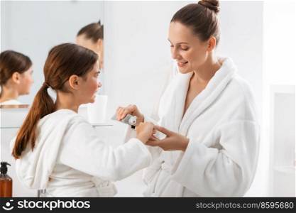beauty, hygiene, morning and people concept - happy smiling mother and daughter applying toothpaste to toothbrush at bathroom. mother and daughter with toothpaste and toothbrush
