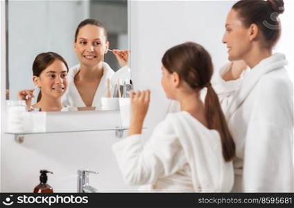 beauty, hygiene, morning and people concept - happy smiling mother and daughter cleaning ears with cotton swabs and looking to mirror at bathroom. mother and daughter cleaning ears with cotton swab