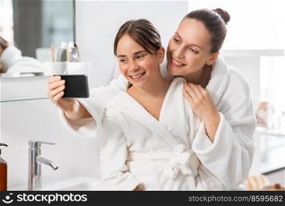 beauty, hygiene, morning and people concept - happy smiling mother and daughter taking selfie with smartphone at bathroom. mother and daughter taking selfie with smartphone
