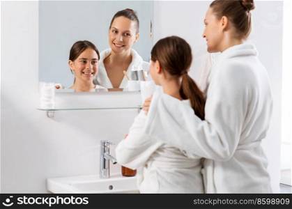 beauty, hygiene, morning and people concept - happy smiling mother and daughter looking to mirror at bathroom. mother and daughter looking to mirror at bathroom