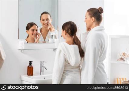 beauty, hygiene, morning and people concept - happy smiling mother and daughter with cotton pads cleaning face skin and looking to mirror at bathroom. mother and daughter with cotton pads cleaning skin