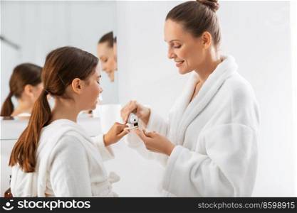 beauty, hygiene, morning and people concept - happy smiling mother and daughter applying toothpaste to toothbrush at bathroom. mother and daughter with toothpaste and toothbrush